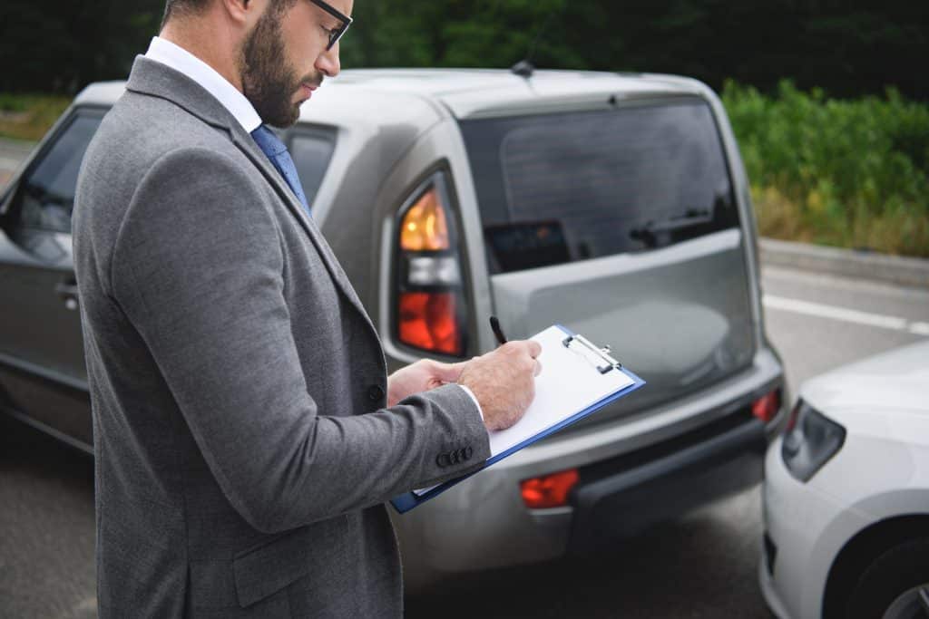 Side View Of Man Writing Something To Car Insurance After Car Accident