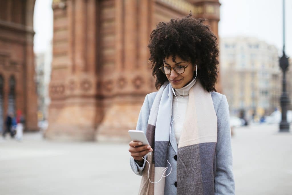 Spain, Barcelona, Smiling Woman With Cell Phone And Earphones In The City