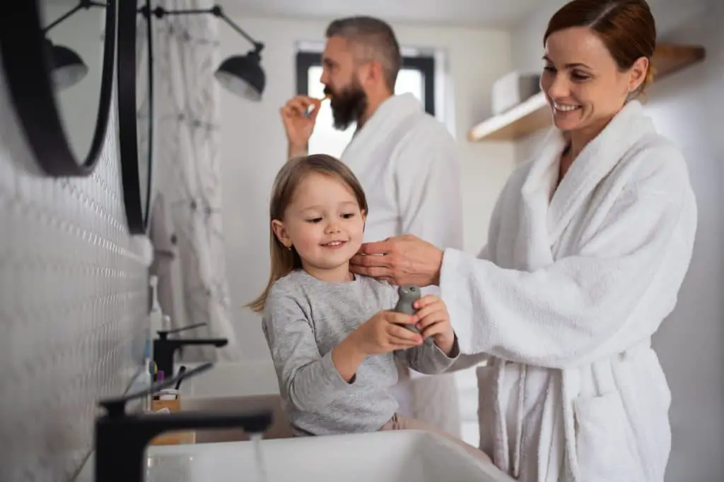 Father And Mother With Small Daughter Washing Indoors In Bathroom In The Evening Or Morning.