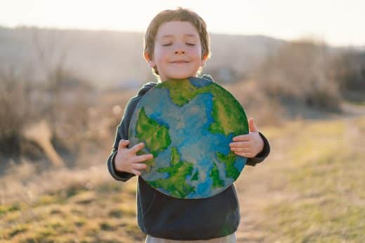 Little Boy Holding Planet In Hands Against Green Spring Background. Earth Day