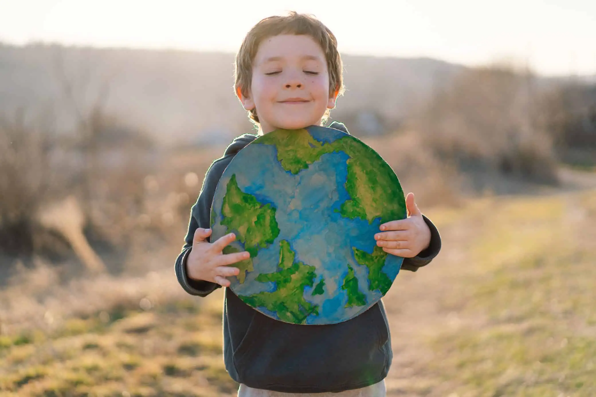 Little Boy Holding Planet In Hands Against Green Spring Background. Earth Day