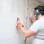 Construction Worker Repairing A Crack, Plastering Cement On Wall. Builder Wearing Safety Gloves, Glasses And Earmuffs.