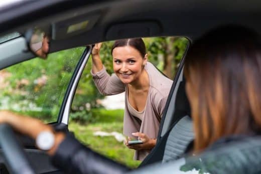 Une femme souriante regarde à l'intérieur d'une voiture à travers la fenêtre ouverte.