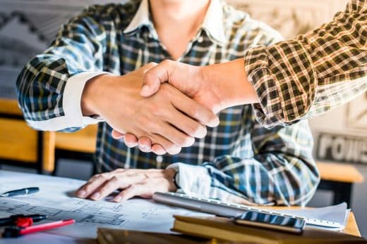 Deux hommes se serrant la main au-dessus de plans de rénovation.