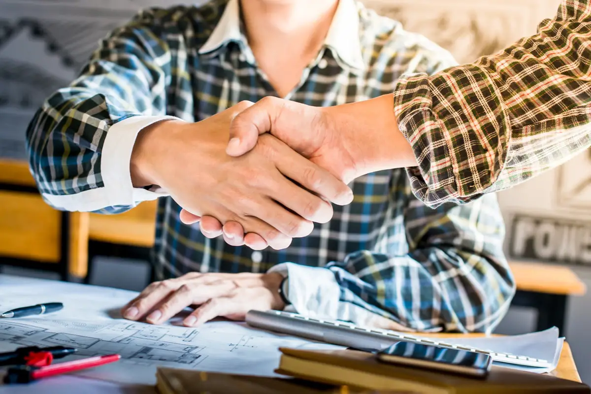 Deux hommes se serrant la main au-dessus de plans de rénovation.