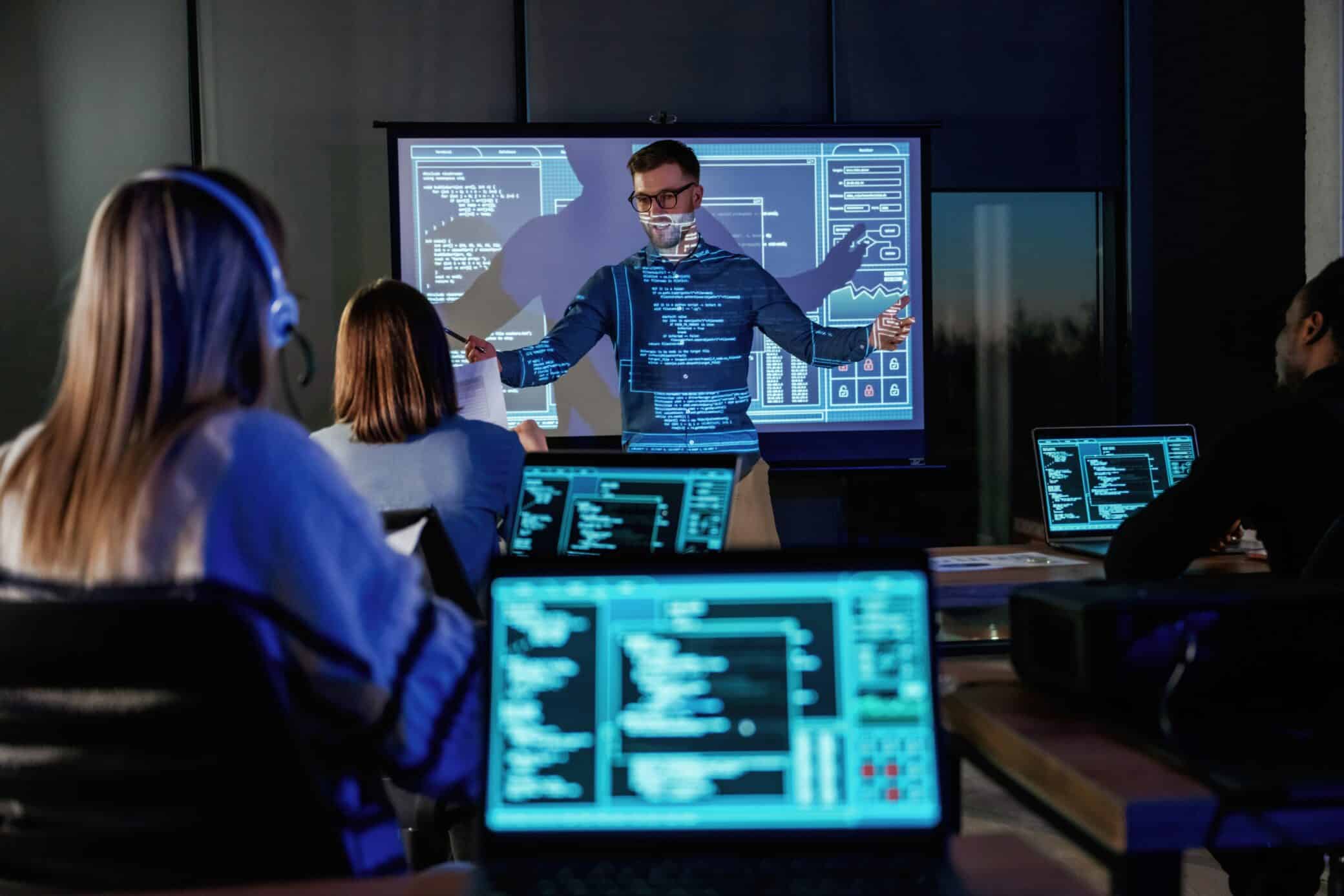 Audience Is With Laptops. Male Business Trainer Is Against Projector With Data, Teaching People