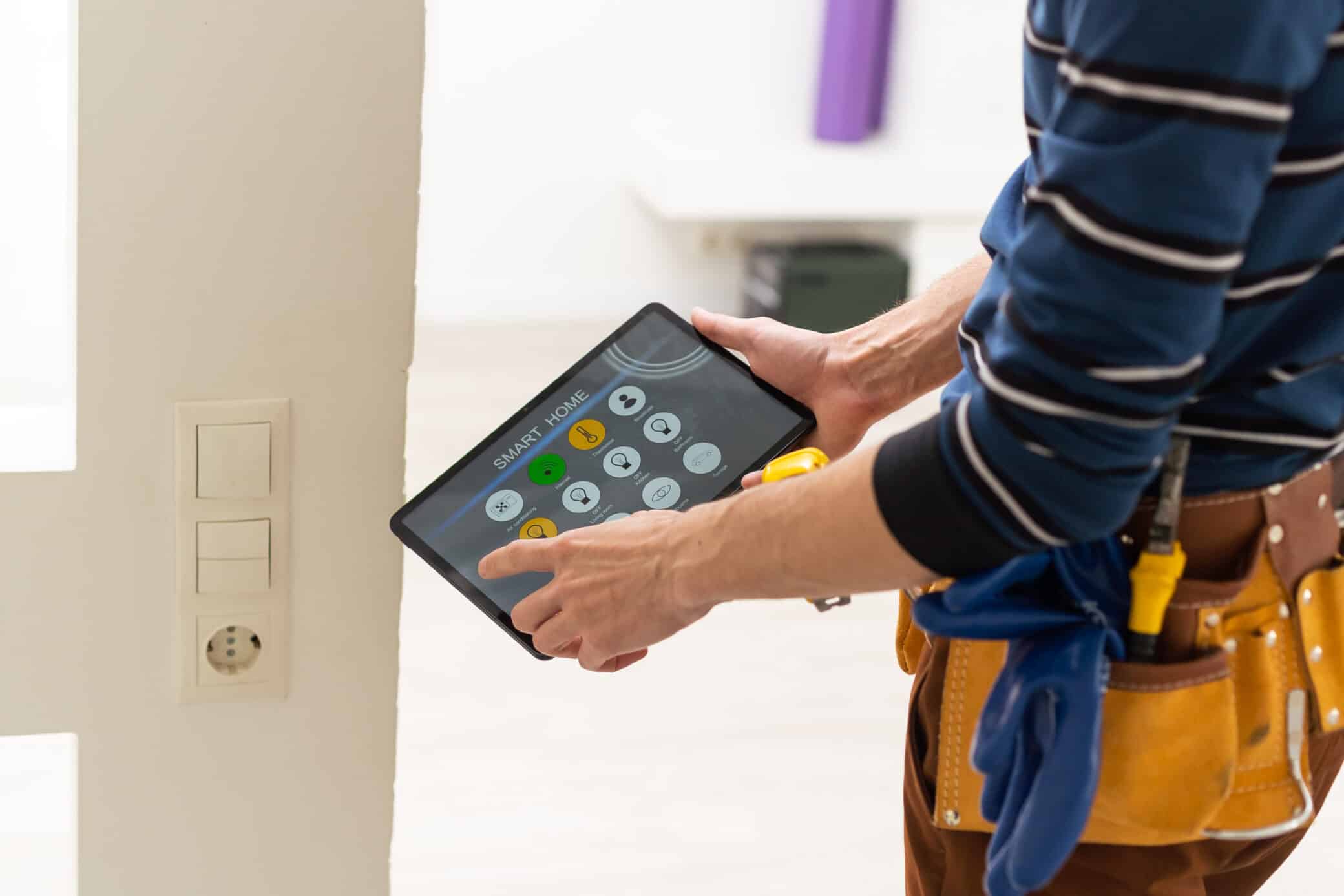 Electrician In Hardhat And Safety Vest Holding Digital Tablet And Fixing Electric Panel
