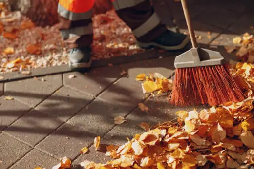 Janitor Cleaner Sweeping Autumn Leaves On The Street.