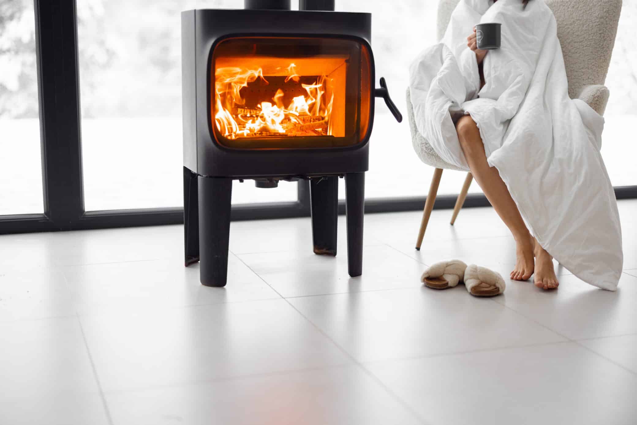 Woman Sitting On Chair By The Burning Fireplace At Home