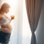 Young Future Mother Standing Near The Window At Home